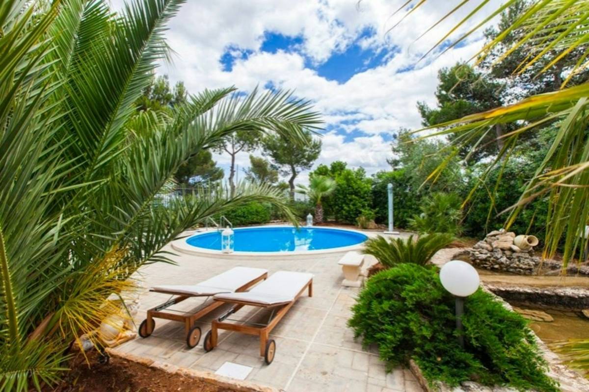 Piscina redonda con tumbonas de madera junto a palmeras